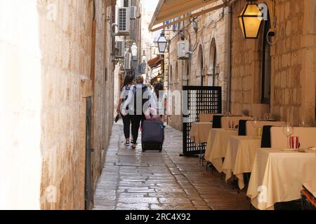 Les voyageurs avec des valises se promènent dans le lieu historique en plein jour. Passage entre les murs de la vieille ville. Été en Croatie, Dubrovnik. Banque D'Images