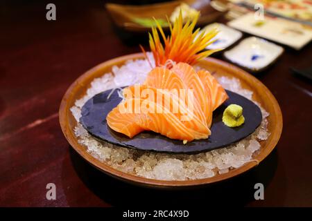Gros plan peu profond de sashimi de saumon magnifiquement disposés sur une dalle de pierre. Il y avait du wasabi à côté. et ornements de fleurs sur des monticules de glace en roun Banque D'Images
