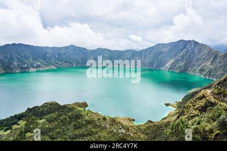 Vue pittoresque de l'eau bleue brillante et ondulante Quilotoa lagune de l'Équateur entourée de montagnes rocheuses et d'arbres verts sous ciel couvert dans la journée Banque D'Images