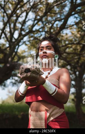 Angle faible de jeune guerrière maya féminine focalisée dans des costumes traditionnels et visage peint tenant la tête de serpent sculptée tout en se tenant dans le parc et regardant Banque D'Images