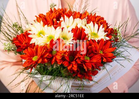 Bouquet de tournesols rouges et blancs frais placés enveloppés dans le journal et tenus par une personne anonyme à la lumière du jour Banque D'Images