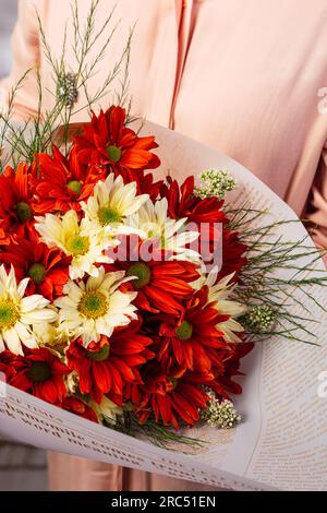 Angle élevé de bouquet de tournesols rouges et blancs frais placés enveloppés dans le journal et tenus par une personne anonyme à la lumière du jour Banque D'Images