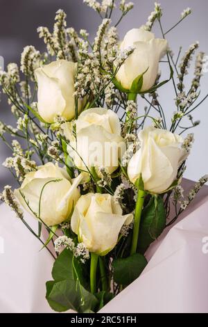 Bouquet de fleurs roses blanches fraîches avec tige fleurie enveloppée dans du papier de décoration placé sur fond gris flou Banque D'Images