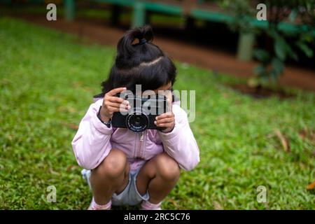 Une jeune fille tient un appareil photo reflex numérique et regarde à travers le viseur, prenant des photos du monde qui l'entoure. Banque D'Images