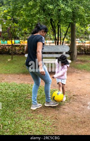 Une heureuse fille de 5 ans et sa mère jouent au football dans le parc. La fille rit et court après le bal Banque D'Images