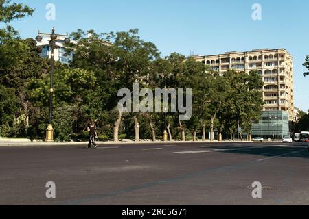 Bakou, Azerbaïdjan - 26 juin 2023 : un piéton solitaire marche dans les rues vides du centre-ville de Bakou, avec un bâtiment historique en toile de fond Banque D'Images