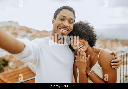 Heureux satisfait Millennial homme afro-américain embrassant la femme avec bague, faisant selfie, appel vidéo Banque D'Images