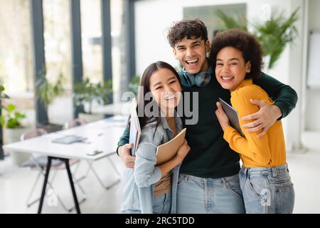 Portrait d'heureux étudiants internationaux amicaux embrassant, posant dans l'espace de coworking, espace libre Banque D'Images