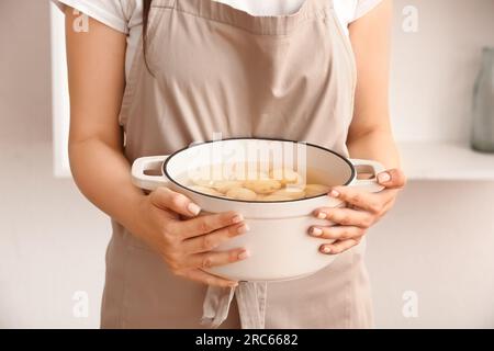 Femme tenant un pot avec des pommes de terre pelées dans la cuisine Banque D'Images
