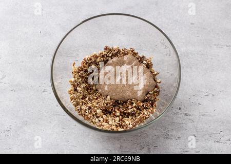 Bol en verre avec un mélange de flocons d'avoine, noix, sucre de coco, dattes et oeuf de lin sur un fond gris texturé, vue de dessus. Cuisson végétalienne de l'oatmea sain Banque D'Images