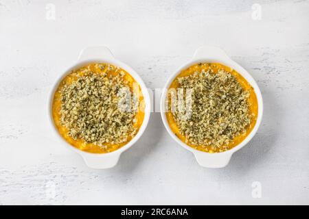 Casserole de citrouille maison ou gratin avec fromage et graines de citrouille dans deux boîtes en céramique sur un fond gris clair, vue de dessus. Banque D'Images