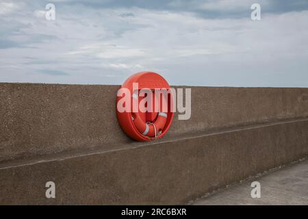 Bouée de sauvetage orange vif attachée à un mur du port contre un ciel orageux Banque D'Images