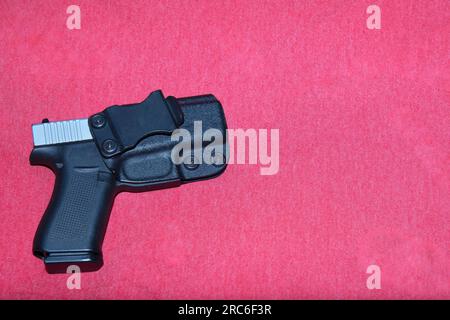 Photo d'un pistolet dans un étui noir sur fond rouge. Banque D'Images