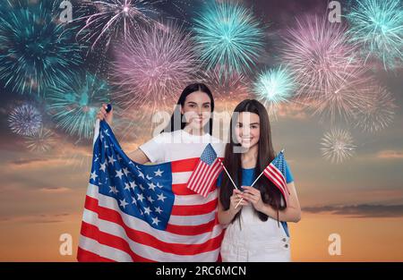 4 juillet - jour de l'indépendance de l'Amérique. Heureuse mère et fille tenant les drapeaux nationaux des États-Unis contre le ciel avec des feux d'artifice Banque D'Images