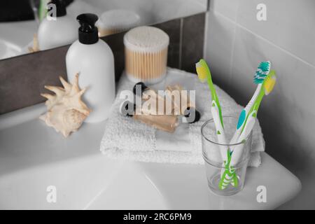 Brosses à dents colorées dans le support en verre et produits cosmétiques sur le lavabo Banque D'Images