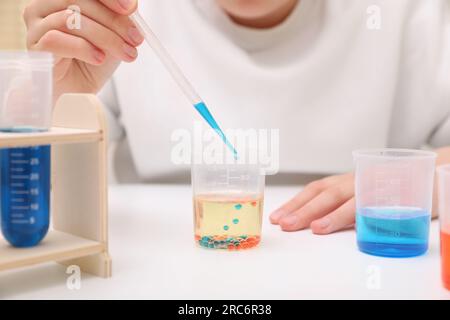 Fille mélangeant des liquides colorés à la table blanche à l'intérieur, gros plan. Kit d'expérimentation chimique pour enfants Banque D'Images