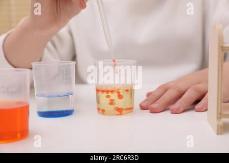 Fille mélangeant des liquides colorés à la table blanche à l'intérieur, gros plan. Kit d'expérimentation chimique pour enfants Banque D'Images