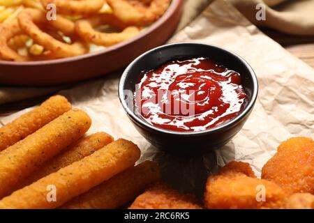 Savoureuses nuggets de poulet, bâtonnets de fromage et ketchup sur papier parchemin, gros plan Banque D'Images