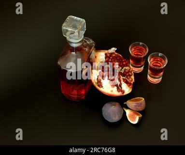 Figue liqueur de grenade sur fond noir, une bouteille et deux verres d'alcool, fruits mûrs à proximité. Vue de dessus, pose à plat. Banque D'Images