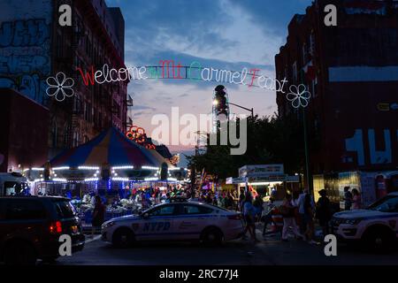 Brooklyn, NY, États-Unis. 12 juillet 2023. Un grand clocher, parsemé de lys et portant une bande, est porté sur les épaules des paroissiens et défilé à travers la paroisse dans le cadre de la fête de notre-Dame du Mont Carmel dans le quartier Williamsburg de Brooklyn. Le clocher, ou « giglio », est rebondi, ou « dansé » dans la rue plusieurs fois pendant la fête de 11 jours, y compris cet « ascenseur de nuit ». Une vue sur North 8th Street, bordée de manèges et de concessions. Crédit : Ed Lefkowicz/Alamy Live News Banque D'Images