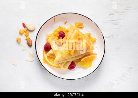 Crêpe française traditionnelle Suzette avec sauce orange dans une assiette blanche sur fond blanc. Vue de dessus. Banque D'Images