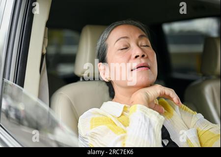 Image en gros plan d'une dame asiatique senior essuyant sa sueur tout en conduisant une voiture pendant une chaude journée d'été. trajet, déplacement, véhicule Banque D'Images