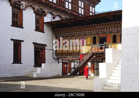 Une paire de moines bouddhistes aux couleurs rouges marchent près d'un bâtiment traditionnel peint coloré sur le terrain de Tashichho Dzong à Thimphu, au Bhoutan. Banque D'Images