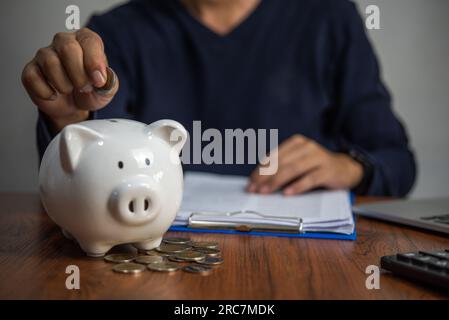 Homme mettant des pièces dans une tirelire. Investissement et économie d'argent, banque et finance, comptabilité et fiscalité concept d'entreprise. Banque D'Images