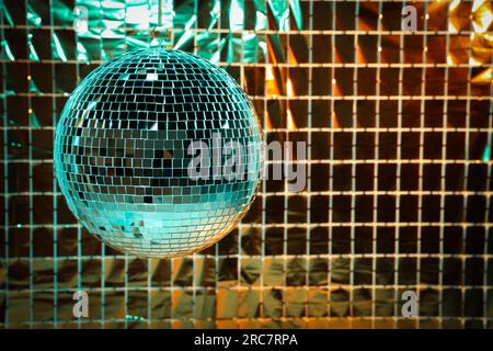 Boule disco brillante contre rideau de fête en aluminium sous la lumière turquoise et orange, espace pour le texte Banque D'Images