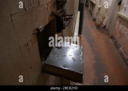 Intérieur du musée KGB dans 'The Corner House' à Riga. Fenêtre pour transférer de la nourriture et observer les prisonniers dans la porte d'une cellule Banque D'Images