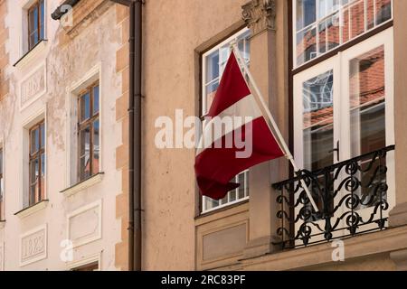 Le drapeau national letton avec deux larges bandes horizontales rouges, séparées par une étroite bande blanche, flotte devant un bâtiment de la capitale Riga Banque D'Images