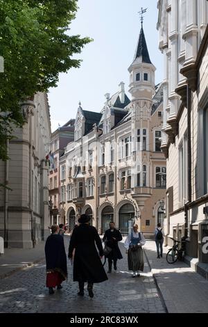 Les gens en costumes traditionnels lettons marchent dans la rue Amatu iela à Riga avec des bâtiments de style art nouveau colorés typiques Banque D'Images