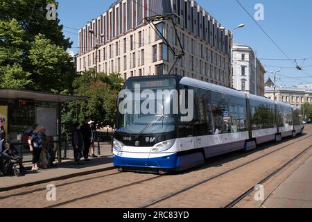 Transports publics Riga. Le tramway électrique bleu et blanc s'arrête à un arrêt où les passagers attendent Banque D'Images