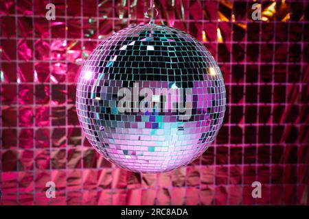 Boule disco brillante contre rideau de fête en aluminium sous la lumière rose Banque D'Images