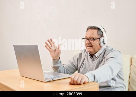 Un homme plus âgé porte un micro-casque commencer la vidéoconférence à la maison. Un ordinateur portable masculin mature accueille un thérapeute en ligne, accueillant des enfants adultes vivant à l'étranger. Distan Banque D'Images