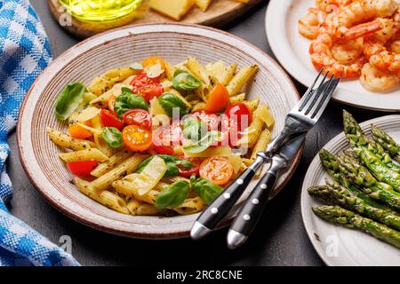 Une délicieuse assiette de pâtes italiennes ornée de tomates fraîches et de feuilles de basilic aromatiques, d'asperges grillées et de crevettes Banque D'Images