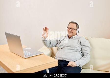 Un homme plus âgé porte un micro-casque commencer la vidéoconférence à la maison. Un ordinateur portable masculin mature accueille un thérapeute en ligne, accueillant des enfants adultes vivant à l'étranger. Distan Banque D'Images
