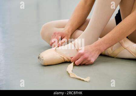 Ballerine mettant sur le ballet pointe chaussures assis sur le sol. Banque D'Images