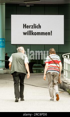 Hambourg, Allemagne. 13 juillet 2023. Deux visiteurs de l'Assemblée générale annuelle de Fielmann Aktiengesellschaft sont accueillis par les mots « Bienvenue ! » sur le lieu de la réunion. L’inflation pousse les clients vers des fournisseurs comme Fielmann lorsqu’il s’agit d’acheter des lunettes. En fin de compte, les ventes au premier semestre ont augmenté de 13% pour atteindre environ 966 millions d'euros. (À dpa « l'inflation pousse les clients à Fielmann - augmentation des ventes de 13 % ») crédit : Markus Scholz/dpa/Alamy Live News Banque D'Images