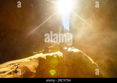 Femme touristique assise sur un rocher avec des effets de soleil légers avec du sable volant dans la gorge naturelle de Standley Chasm, West MacDonnell Ranges. Australien Banque D'Images