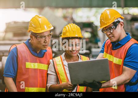 Femme travailleuse d'ingénieur avec l'équipe masculine travaillant ensemble dans l'usine regardant l'ordinateur portable sourire heureux. Banque D'Images