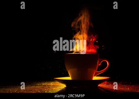 Un mug avec une boisson chaude et de la vapeur bouclés se lève, illuminé en rouge-jaune, orange sur fond noir, espace de copie, créatif, silhouette. Matin Banque D'Images