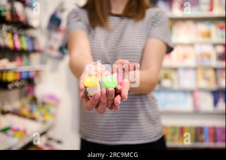 Gros plan de petites bouteilles avec des peintures acryliques colorées vibrantes dans les mains d'une vendeuse féminine dans une boutique d'art. Magasin de papeterie scolaire. Magasin de fournitures de bureau. P Banque D'Images