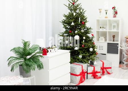 Grands cadeaux couchés sous un sapin de Noël décoré dans une pièce lumineuse Banque D'Images