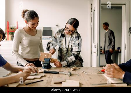 Enseignant aidant l'étudiante adolescente tout en coupant du bois pendant le cours de menuiserie Banque D'Images