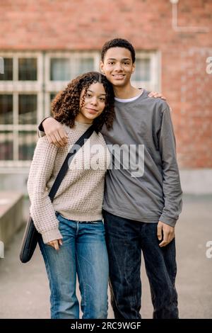 Portrait d'un adolescent souriant, homme et femme, debout avec les bras autour sur le campus du lycée Banque D'Images