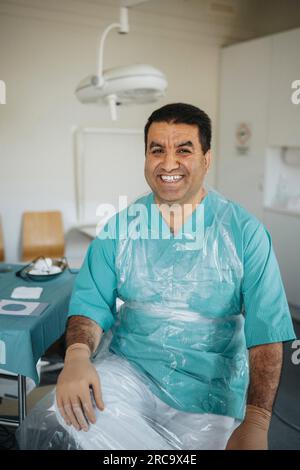 Portrait d'un chirurgien masculin souriant portant une assise protectrice en salle d'examen médical Banque D'Images