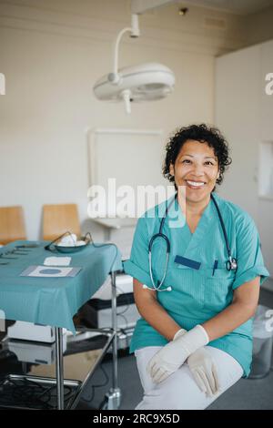 Portrait de femme médecin heureuse portant des gommages médicaux assis dans la salle d'examen médical Banque D'Images