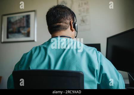 Vue arrière d'un médecin portant un casque à l'aide d'un ordinateur lors d'une consultation en ligne Banque D'Images