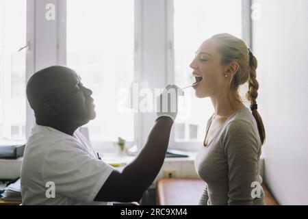 Vue latérale du médecin masculin examinant la bouche d'une patiente en clinique Banque D'Images